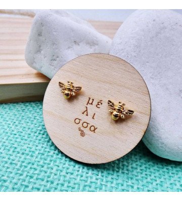 Women gold plated bee earrings on woden plate.